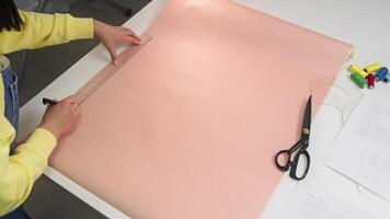Designer begins by creating a drawing for the future garment on specialized pink paper, making notes as they go. High angle video
