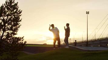 Young man and a woman give each other high fives in the park, with the setting sun as a backdrop. Slow motion video