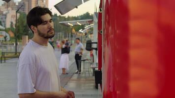 Young guy is at a food stand, trying to decide what to get. He's starving and just wants something to eat. Slow motion video