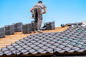 laborer with a chainsaw on the roof of a family house, building a roof from fired ceramic tiles photo