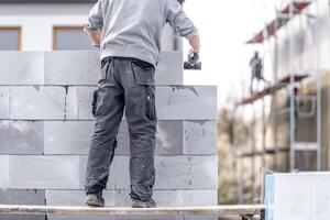 a mason builds the wall of a building from concrete bricks and blocks photo
