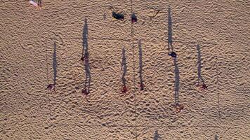 Aerial view. Tourists play beach volleyball at sunset. The shadows of the players create interesting figures in the sand. Beach sports video