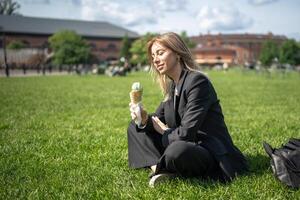 contento sonriente mujer en disfraz traje comiendo hielo crema, relajante sentado en césped en naturaleza parque. foto