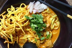 A bowl of Khao Soi, a Northern Thai noodle soup featuring egg noodles bathed in a fragrant coconut curry broth, topped with crispy noodles, pickled mustard greens, and fresh cilantro. photo