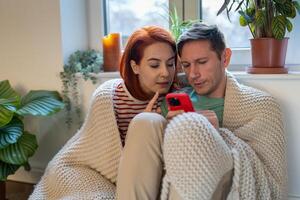 Young married couple sitting on floor, man holding smartphone and discussing order in online store photo
