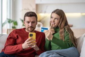 Happy married couple spouses shopping online via internet using smartphone, sitting on couch. photo