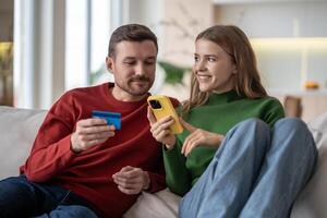 Online home shopping. Interested couple pays for purchases with bank card using phone sits on couch. photo
