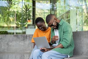 Cheerful joyful african american friends, woman, man studying with computer outdoor together photo