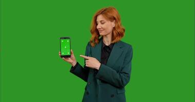 Woman pointing to mock up smartphone with aproval over green screen background. video