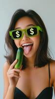 A cheerful girl poses with a cucumber and quirky sunglasses, radiating fun photo
