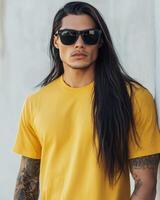 A stylish model wearing a plain t-shirt stands confidently against a wall photo