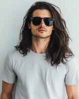 un elegante joven hombre poses con confianza en un blanco camiseta y Gafas de sol foto