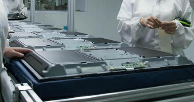 Workers in protective gowns and gloves assemble computer monitors on a conveyor belt. video