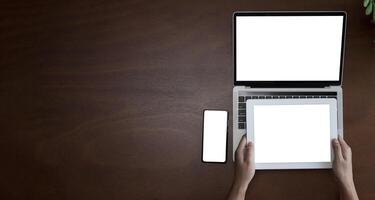 Top view of businesswoman sitting at white desk and uses smartphone on table are laptop and digital tablet with blank screen.Girl using gadget. photo