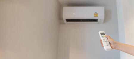 The white air conditioner remote is being used by a human hand to turn on and adjust the air conditioner in a room. Adjusting temperature of air conditioner by remote. photo