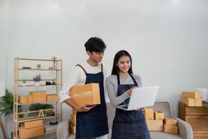 Young Couple Selling Products Online from Home Using Laptop and Packing Boxes for Shipping photo