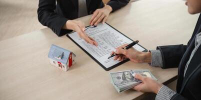 Real Estate Agents Discussing Home Buying and Selling Contracts with Money and Model House on Desk photo