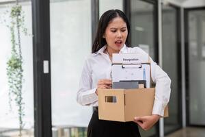 Young Female Office Worker Holding a Box with Resignation Document, Expressing Emotion in Modern Office Setting photo