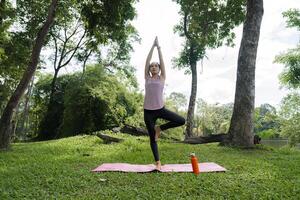Young Woman Practicing Yoga in a Serene Park Setting Surrounded by Lush Greenery and Trees photo