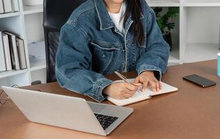 Young Woman Studying Online from Home Using Laptop and Taking Notes in a Notebook at a Modern Workspace photo