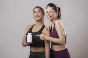 Two Female Models Are Standing With One Holding Pill Bottle While Another Points Her Finger At The Bottle photo