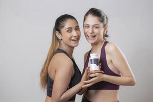 Two Of The Hottest Models Are Smiling And Looking At The Camera While Holding A Medicine Bottle photo
