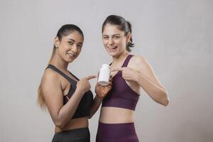 Two Cute Females Are Pointing Their Fingers At A Tablet Bottle While Looking At The Front Camera photo