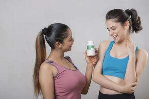 Two Beauty Ladies Are Looking Lovingly At The Tablet Bottle That One Of Them Is Holding In Her Hand photo