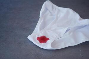 A CloseUp View of White Underwear Featuring a Red Stain Displayed on a Gray Surface photo