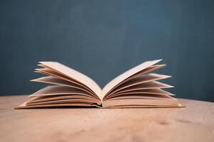 An open book with its pages gently turning rests on a wooden table in the breeze photo