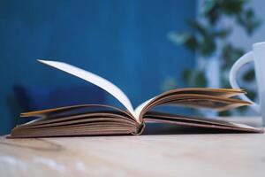 An open book with its pages gently turning rests on a wooden table in the breeze photo