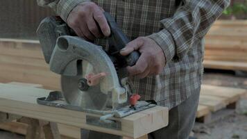 Close-up of an elderly man's hands with a circular saw. The man skillfully operates a circular saw to cut wood in an outdoor workshop. video