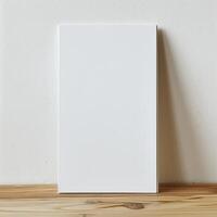 A blank canvas stands on a wooden table against a beige wall in the background. photo