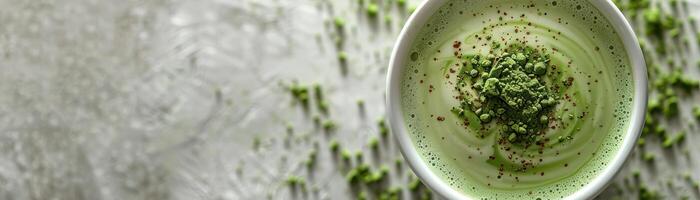 Matcha green tea latte in a white cup on a gray background with matcha powder spilled next to it. photo