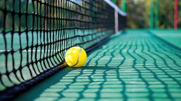 A yellow tennis ball is lying on the ground next to a tennis net. photo