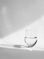 A glass half full of water on a white table with a white background. photo