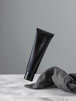 A black tube of face cream is suspended in mid-air above a gray cloth. photo
