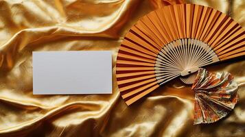 A mockup of a blank business card lying on golden Japanese silk, next to it lies a dancing Japanese fan photo