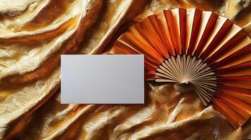 A mockup of a blank business card lying on golden Japanese silk, next to it lies a dancing Japanese fan photo