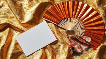 A mockup of a blank business card lying on golden Japanese silk, next to it lies a dancing Japanese fan photo