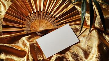 A mockup of a blank business card lying on golden Japanese silk, next to it lies a dancing Japanese fan photo