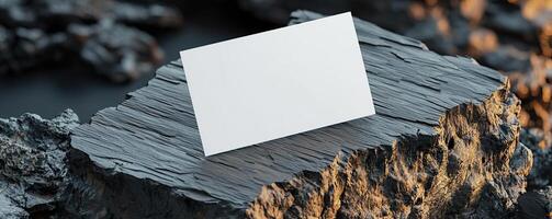 a composition of blank white business card hovering partially over a surface The surface is slab of dark rock and wood on a split color background The card is center and in focus o photo