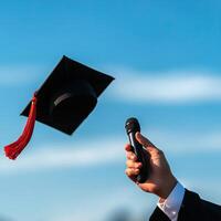 A graduate celebrating success by throwing a cap into the sky while holding a microphone, symbolizing achievement and joy. photo