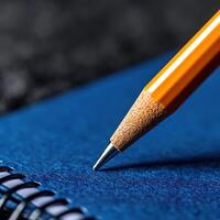 Close-up shot of an orange pencil resting on a blue notebook, highlighting creativity and inspiration in a study environment. photo