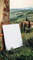 A close up center shot of a blank white 23 A4 piece of art paper leaning up against a building in the greenish fields of Tuscany photo