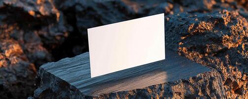 a composition of blank white business card hovering partially over a surface The surface is slab of dark rock and wood on a split color background The card is center and in focus o photo