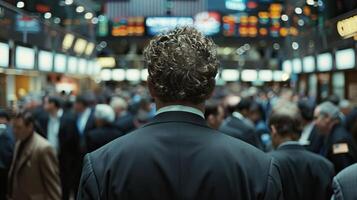 A man in a suit stands alone in a crowded trading room, looking at the large screens displaying stock prices. photo