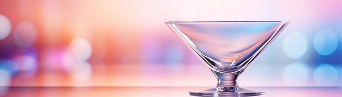 An empty martini glass sits on a glass table against a blurred background of pink and blue lights. photo