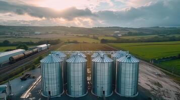 group of grain silos next to a railroad track with the countryside in the background. photo