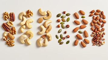 A variety of nuts and seeds are arranged in a row on a white background. There are pistachios, cashews, almonds, pumpkin seeds, and sunflower seeds. photo